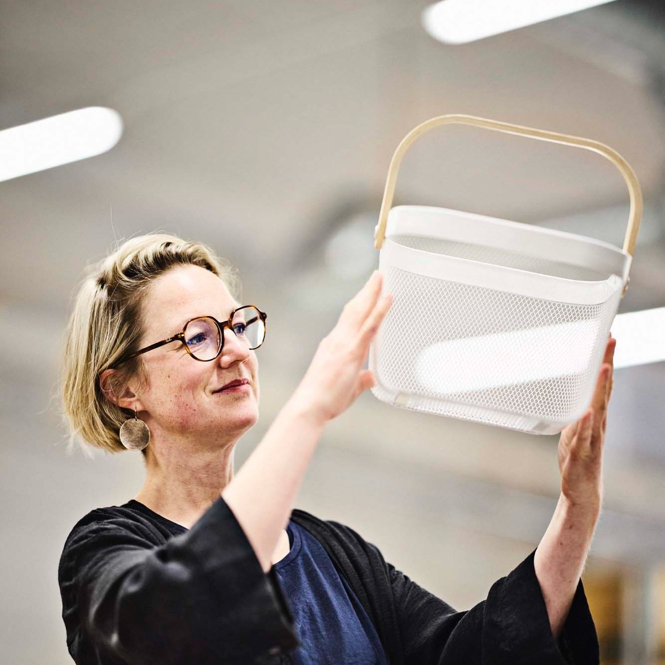IKEA designer Wiebke Braasch looks at a white RISATORP basket held up in her hands.
