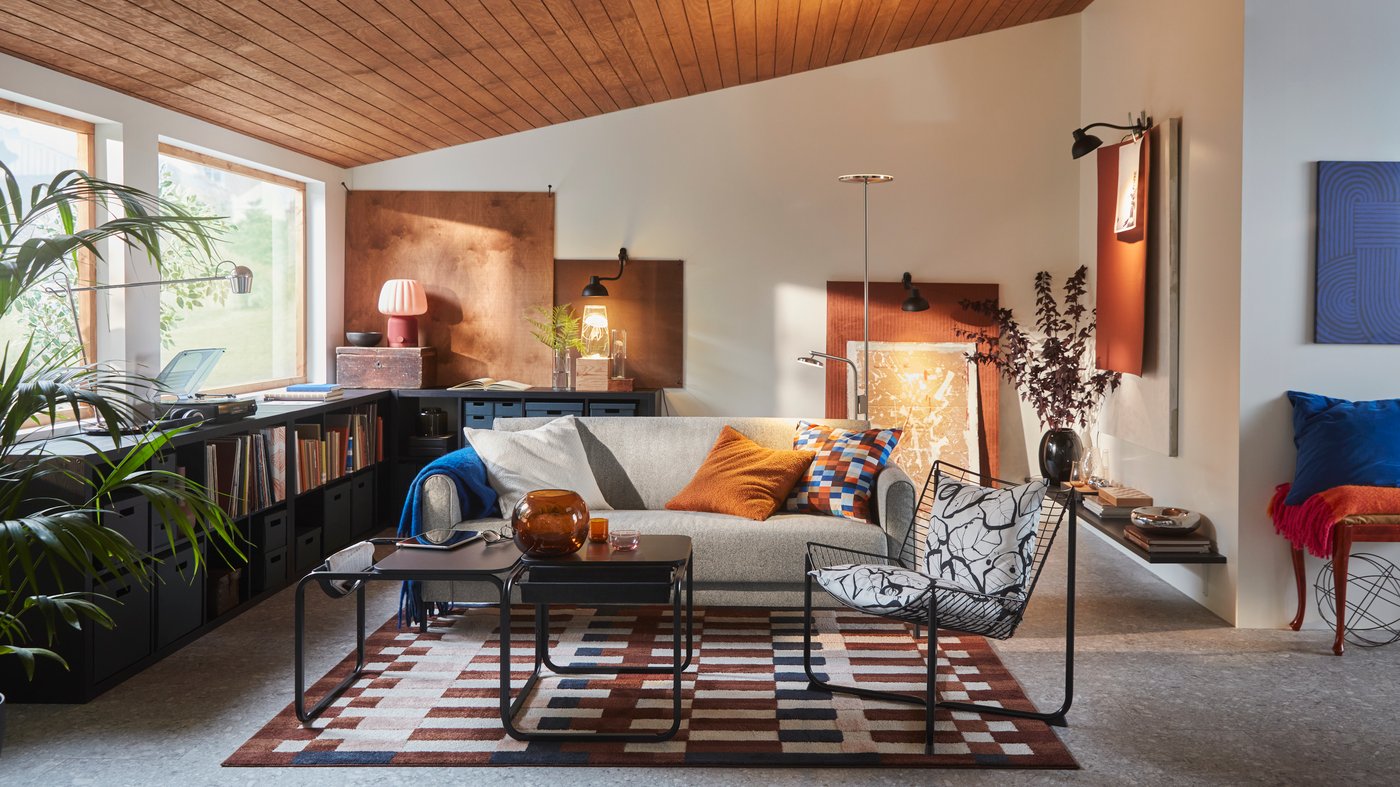 A neutral coloured living room with a wood ceiling, colour block paintings on the wall and colourful decorative textiles.