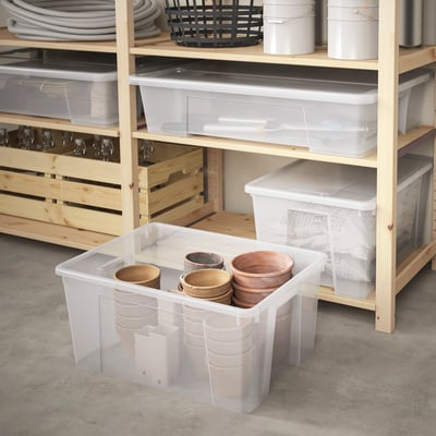 Large transparent SAMLA storage box on shelf with wooden cups, surrounded by similar boxes and items on shelves.